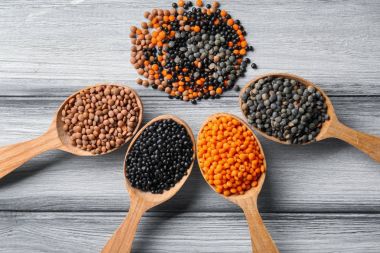 Ahşap arka plan üzerinde farklı mercimek kaşıklarla