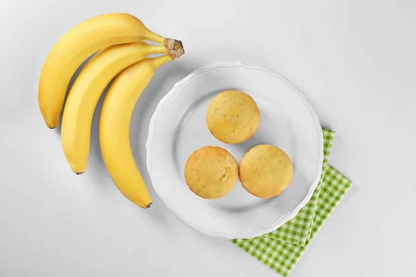 Bananas frescas y plato con magdalenas sobre fondo blanco — Foto de Stock