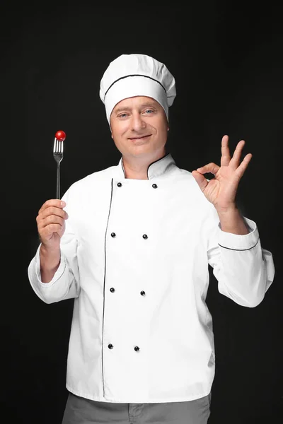 Chef masculino en uniforme sujetando tenedor con tomate cherry sobre fondo negro —  Fotos de Stock