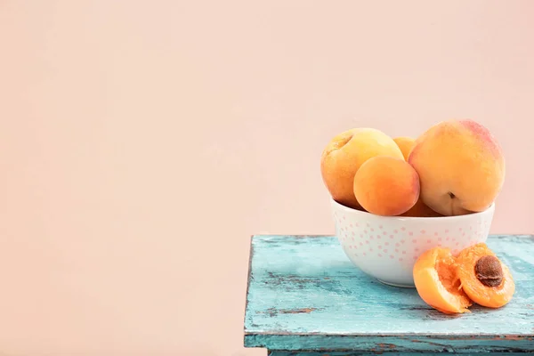 Ripe apricots and ceramic bowl on wooden table — Stock Photo, Image