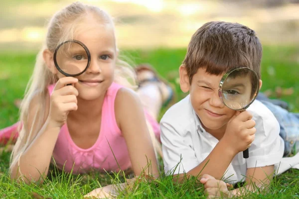 Petits enfants mignons avec loupes couchés sur l'herbe verte dans le parc — Photo