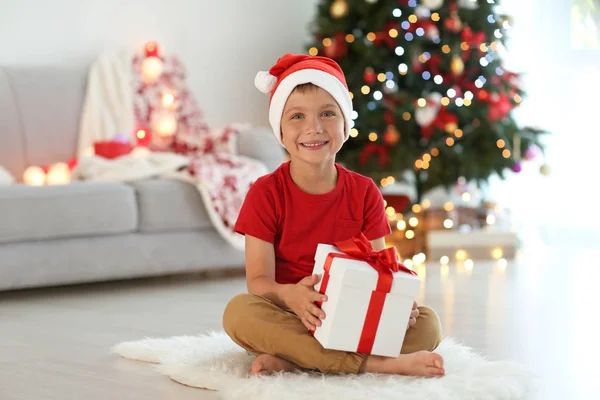 Buon bambino con scatola regalo di Natale seduto su tappeto a casa — Foto Stock