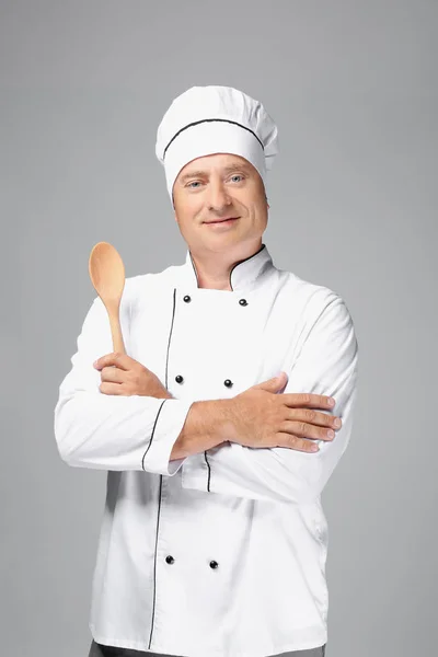 Мужчина шеф-повар в форме держит деревянную ложку на сером фоне — стоковое фото