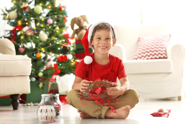 Niedlicher Junge schmückt Weihnachtskranz auf dem Fußboden — Stockfoto