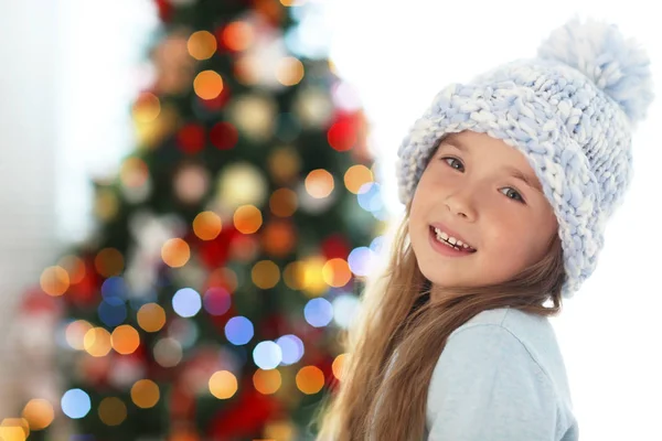 Feliz niña con sombrero contra el borroso árbol de Navidad —  Fotos de Stock