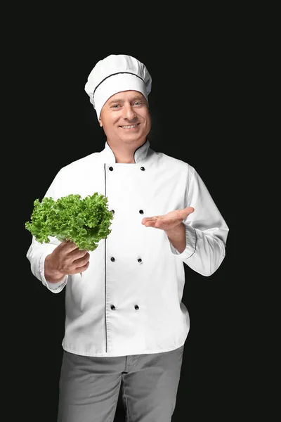 Chef masculino en uniforme sosteniendo ensalada verde sobre fondo negro —  Fotos de Stock