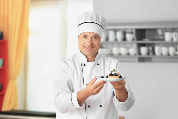 Мужчина шеф-повар держит тарелку с десертом на кухне — стоковое фото