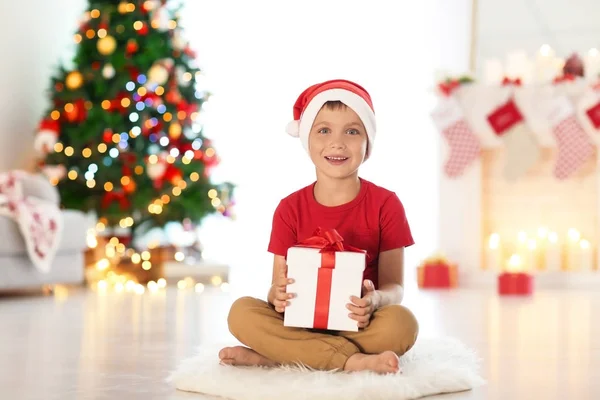 Glad liten pojke med jul presentbox sitter på mattan hemma — Stockfoto