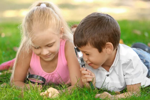 Niedliche kleine Kinder mit Lupen liegen auf grünem Gras im Park — Stockfoto