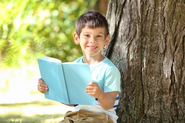 Parkta, ağacın yanında kitap okuyan sevimli bir çocuk.