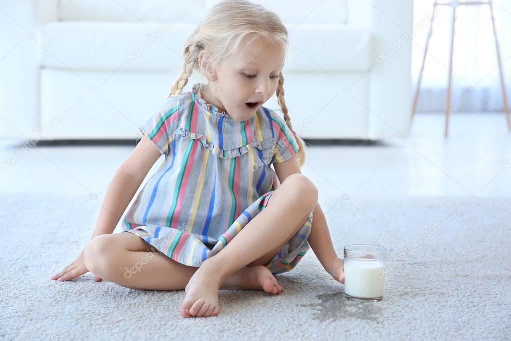 Cute little girl with glass of milk sitting on carpet near wet spot