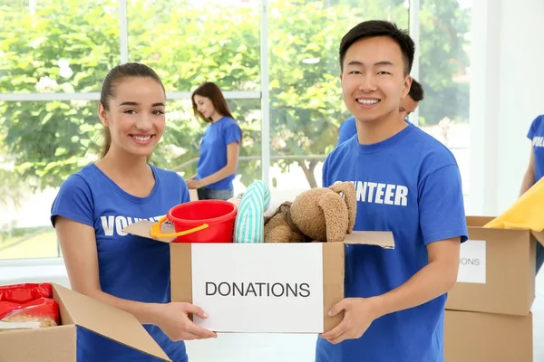 Dos voluntarios adolescentes felices sosteniendo caja de donación en el interior — Foto de Stock