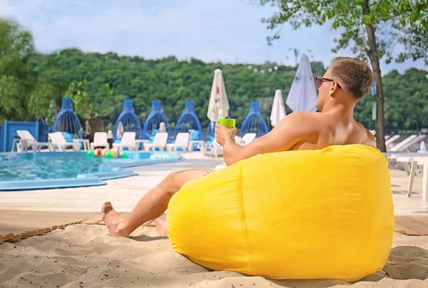 スイミング プールのそばの豆袋の椅子で休んで魅力的な男性 — ストック写真