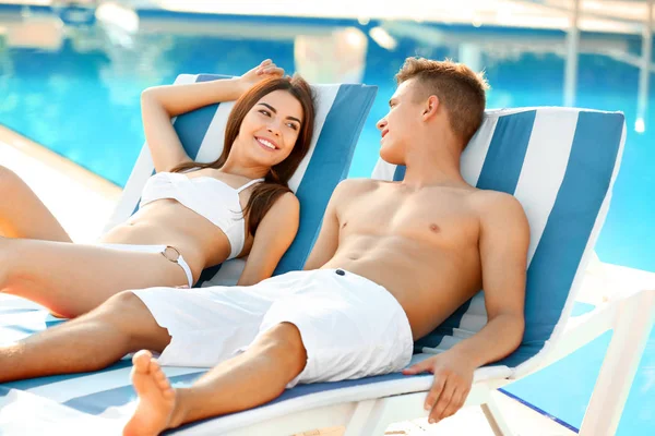 Glückliches junges Paar ruht sich in der Nähe von Schwimmbad im Resort aus — Stockfoto