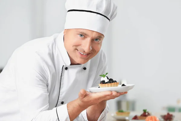Мужчина шеф-повар держит тарелку с десертом на кухне — стоковое фото
