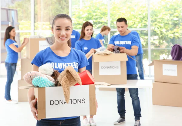 Happy teen volunteer girl holding box with donated toys indoors — Stock Photo, Image