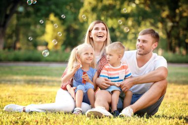 Mutlu aile sabun köpüğü parkta güneşli günde üfleme.