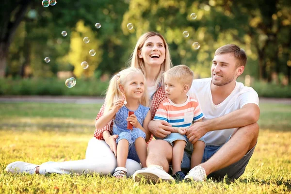 Szczęśliwa rodzina dmuchanie baniek mydlanych w parku na słoneczny dzień — Zdjęcie stockowe
