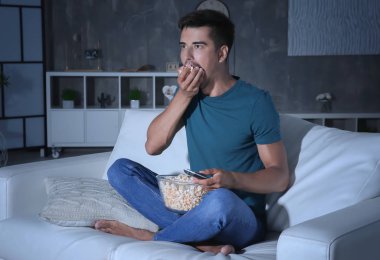 Genç adam yeme patlamış mısır Tv kanepe üzerinde gece izlerken