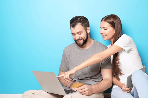 Pasangan muda dengan laptop dan komputer tablet dekat dinding warna. Konsep belanja internet — Stok Foto