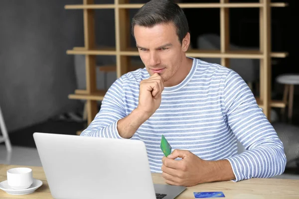 Jeune homme tenant une carte de crédit tout en utilisant un ordinateur portable à la maison — Photo