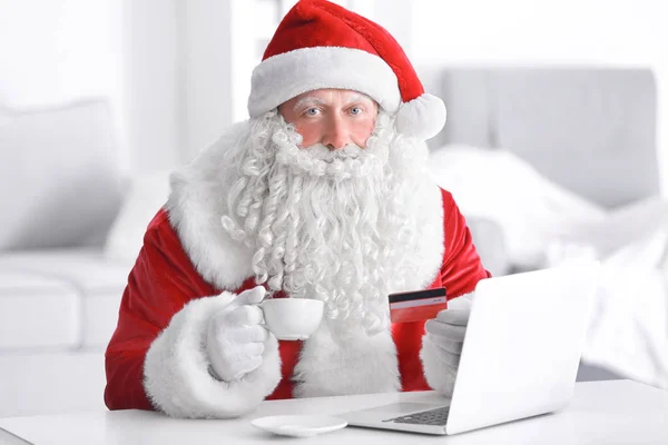 Papai Noel com laptop e cartão de crédito beber café em casa — Fotografia de Stock