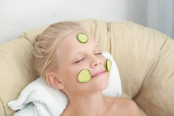 Menina bonito pouco com fatias de pepino no rosto relaxante na poltrona — Fotografia de Stock