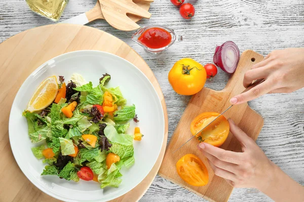 Mujer cortando tomates para ensalada de col rizada en la mesa — Foto de Stock