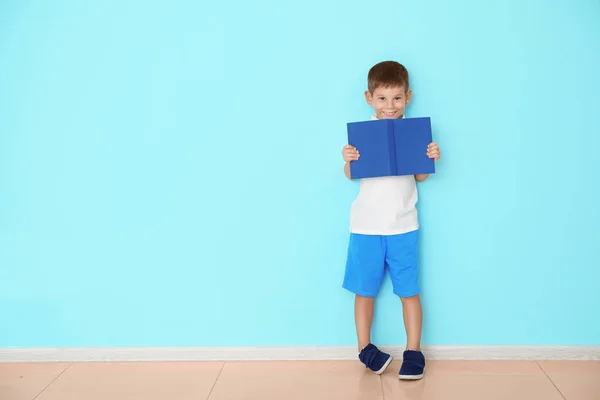 Schattige kleine jongen met boek in de buurt van kleur muur — Stockfoto