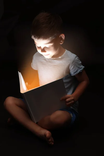 Bonito menino lendo livro na escuridão — Fotografia de Stock