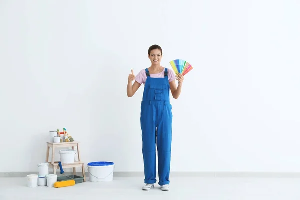 Decorador femenino sosteniendo muestras de paleta de colores cerca de la pared blanca en interiores — Foto de Stock