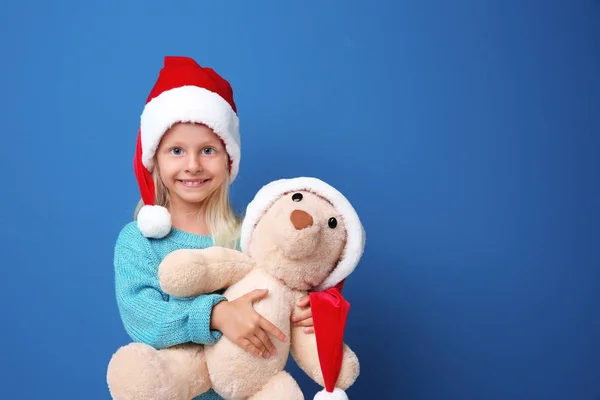 Niedliches Mädchen in Weihnachtsmann-Hut mit Spielzeug auf farbigem Hintergrund — Stockfoto