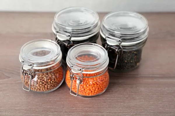 Diferentes tipos de lentilhas em frascos de vidro na mesa de madeira — Fotografia de Stock