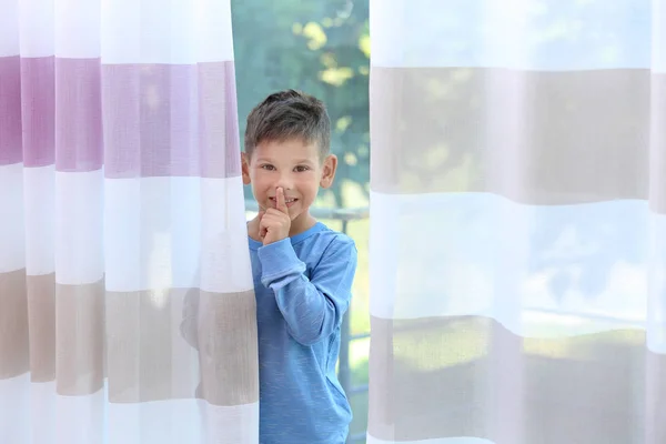 Cute little boy hiding behind curtains at home
