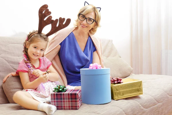 Cute girl and grandmother with Christmas presents on sofa at home — Stock Photo, Image