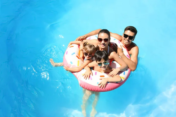 Família feliz com donut inflável na piscina — Fotografia de Stock