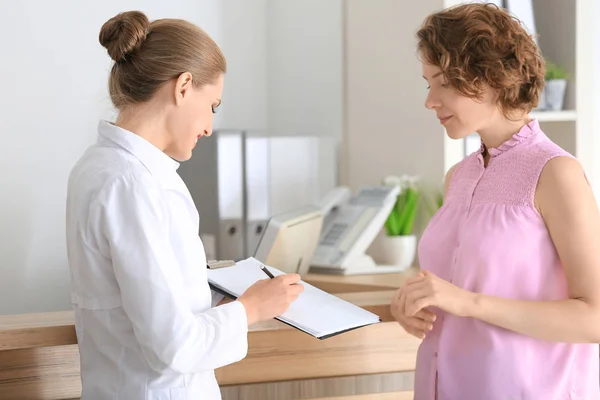 Jonge vrouwelijke receptioniste met client in ziekenhuis — Stockfoto