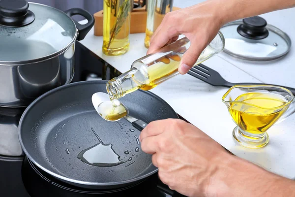 Человек наливает масло из бутылки в ложку на сковородку — стоковое фото
