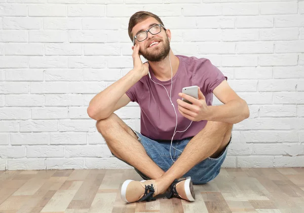 Joven escuchando música mientras está sentado cerca de la pared blanca —  Fotos de Stock