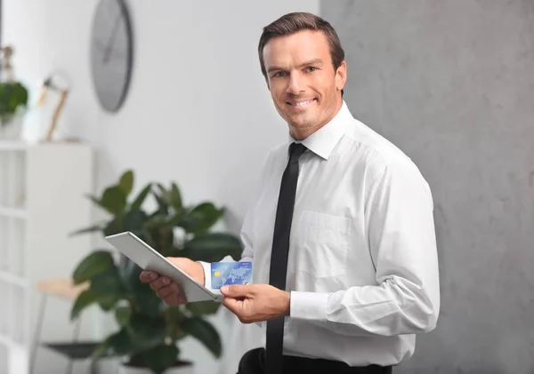 Jeune homme d'affaires tenant une carte de crédit lors de l'utilisation de la tablette au bureau — Photo