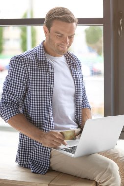 Kredi kartı dizüstü evde kullanırken tutan genç adam