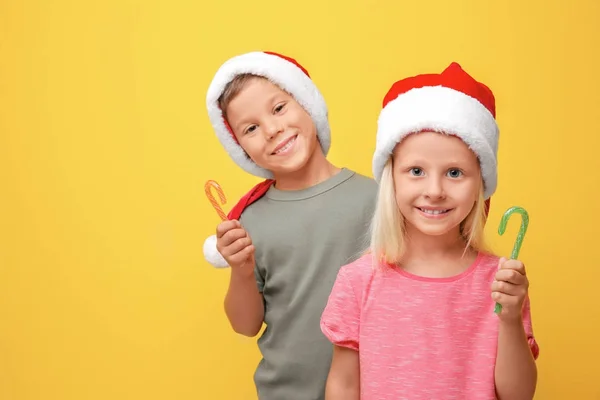 Aranyos gyerekek Santa kalap édességet pálcák színes háttérrel — Stock Fotó