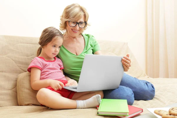 Jolie fille et grand-mère avec ordinateur portable sur le canapé à la maison — Photo