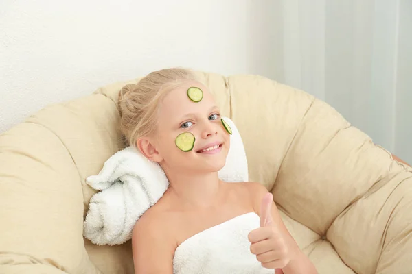 Menina bonito pouco com fatias de pepino no rosto relaxante na poltrona — Fotografia de Stock