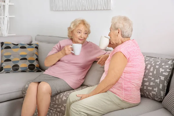 Пожилые женщины пьют кофе, сидя дома на диване — стоковое фото