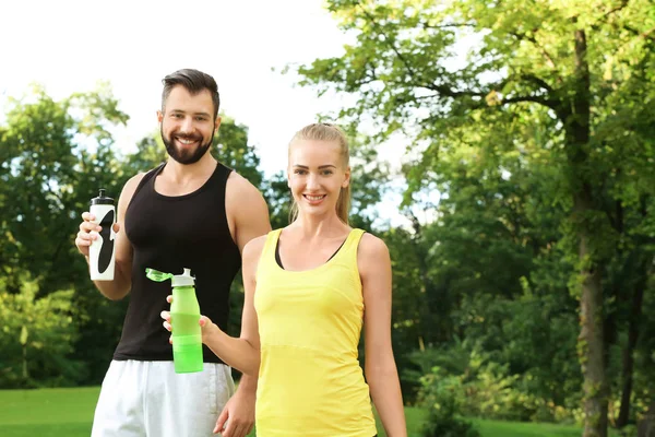 Jong sportief stel met flessen water in groen park — Stockfoto