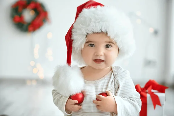 Little baby in Santa hat with Christmas balls on blurred background — Stock Photo, Image