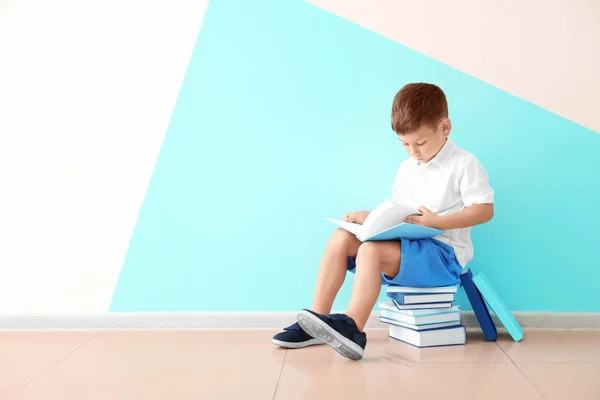 Lindo niño leyendo libros cerca de la pared de color — Foto de Stock