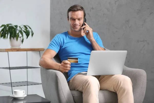 Młody człowiek rozmawia telefon trzymając kartę kredytową w domu — Zdjęcie stockowe
