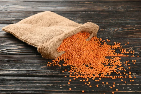 Sackcloth bag with red lentils on wooden background — Stock Photo, Image